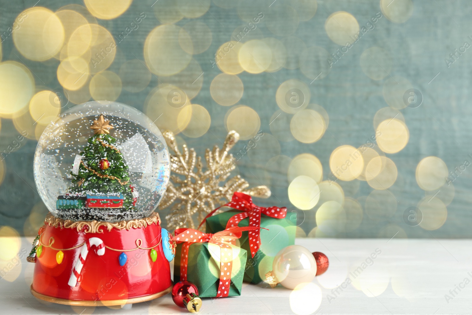 Image of Beautiful Christmas snow globe, gift boxes and decor on light table, bokeh effect. Space for text