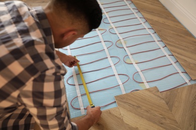 Photo of Professional worker installing electric underfloor heating system indoors
