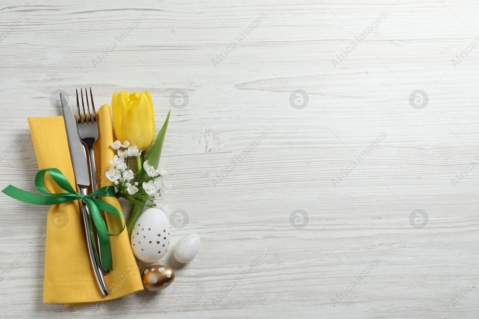 Photo of Cutlery set, Easter eggs and beautiful flowers on white wooden table, flat lay. Space for text