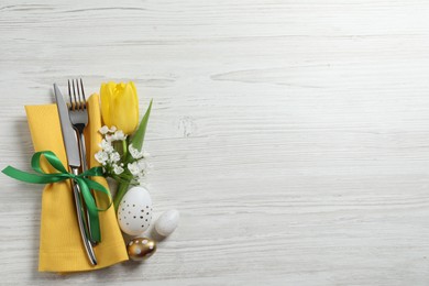 Cutlery set, Easter eggs and beautiful flowers on white wooden table, flat lay. Space for text