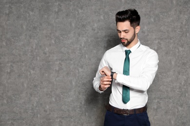 Portrait of confident businessman looking at wristwatch on grey background. Space for text