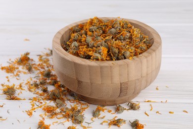 Photo of Bowl with dry calendula flowers on white wooden table, closeup