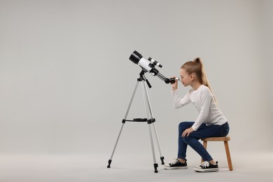 Little girl looking at stars through telescope on light grey background, space for text