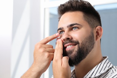 Photo of Young man putting in contact lens indoors