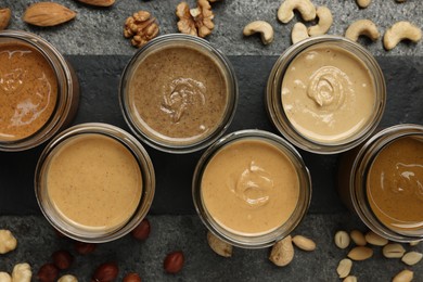 Tasty nut butters in jars and raw nuts on gray table, flat lay