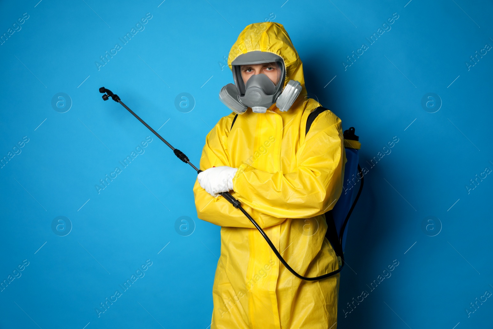 Photo of Man wearing protective suit with insecticide sprayer on blue background. Pest control