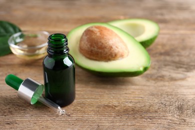 Bottle of essential oil, pipette and fresh avocado on wooden table, space for text