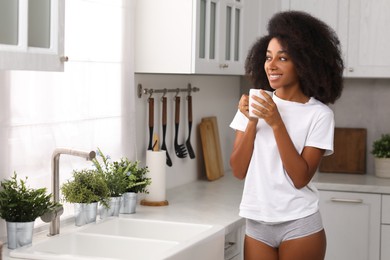 Photo of Beautiful woman in stylish underwear and t-shirt holding cup of drink indoors