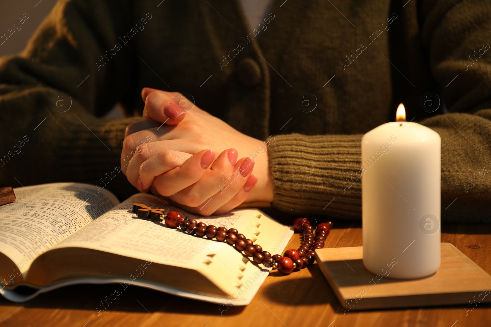 Photo of Woman praying at table with burning candle and Bible, closeup