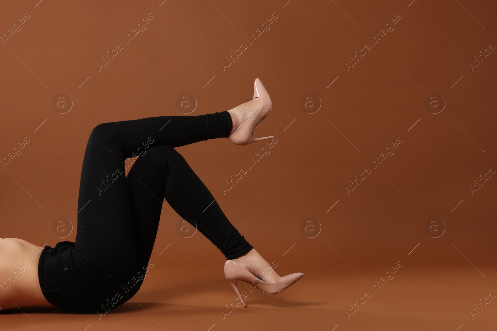 Photo of Woman wearing stylish black jeans and high heels shoes on brown background, closeup. Space for text