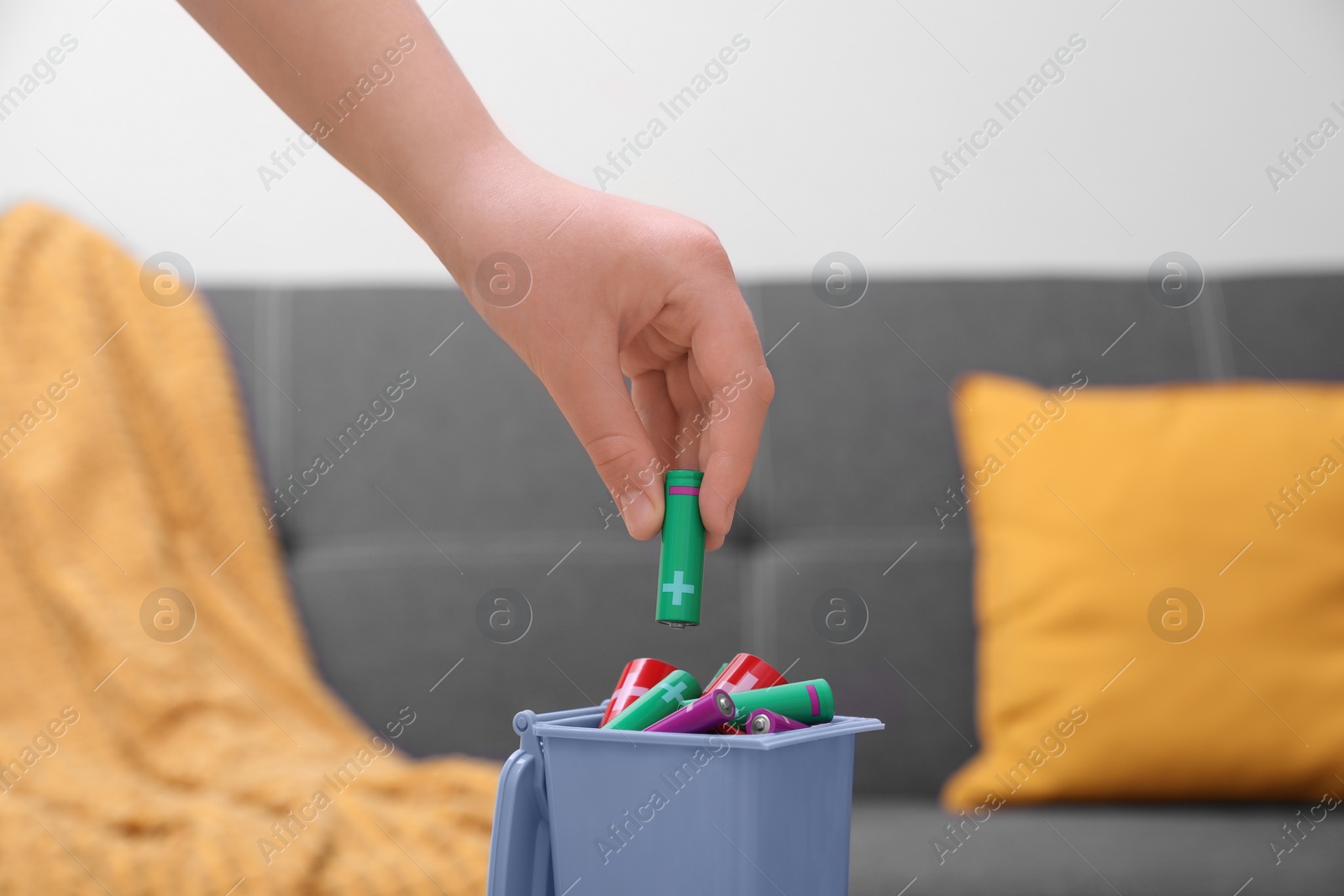 Photo of Woman putting battery into mini recycling bin indoors, closeup
