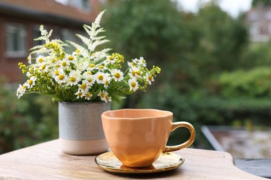 Cup of delicious chamomile tea and fresh flowers outdoors. Space for text