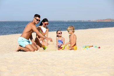 Photo of Happy family playing on sandy beach near sea. Summer holidays