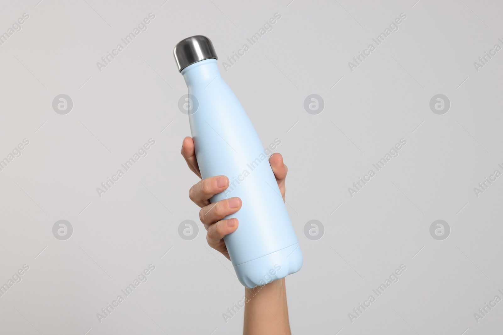 Photo of Woman holding thermo bottle of drink on light background, closeup