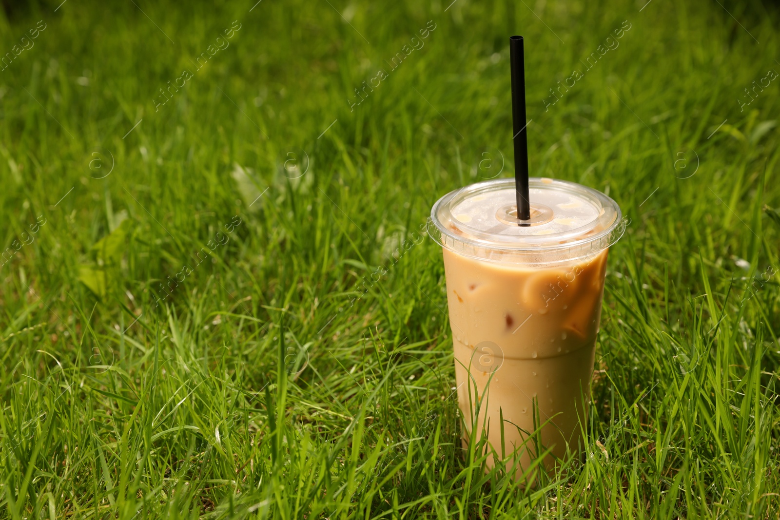 Photo of Takeaway plastic cup with cold coffee drink and straw on green grass outdoors, space for text