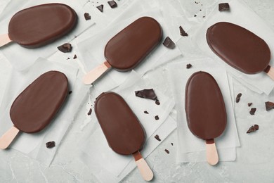 Glazed ice cream bars and chocolate chunks on light grey table, flat lay