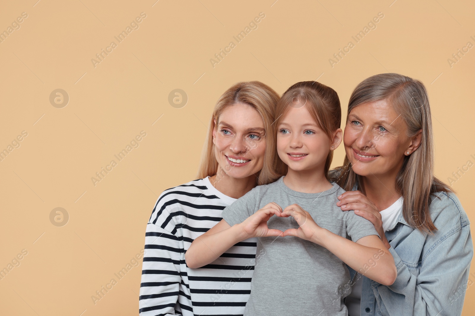Photo of Three generations. Happy grandmother, her daughter and granddaughter making heart with hands on beige background, space for text