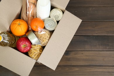 Photo of Cardboard box with donation food on wooden table, top view. Space for text