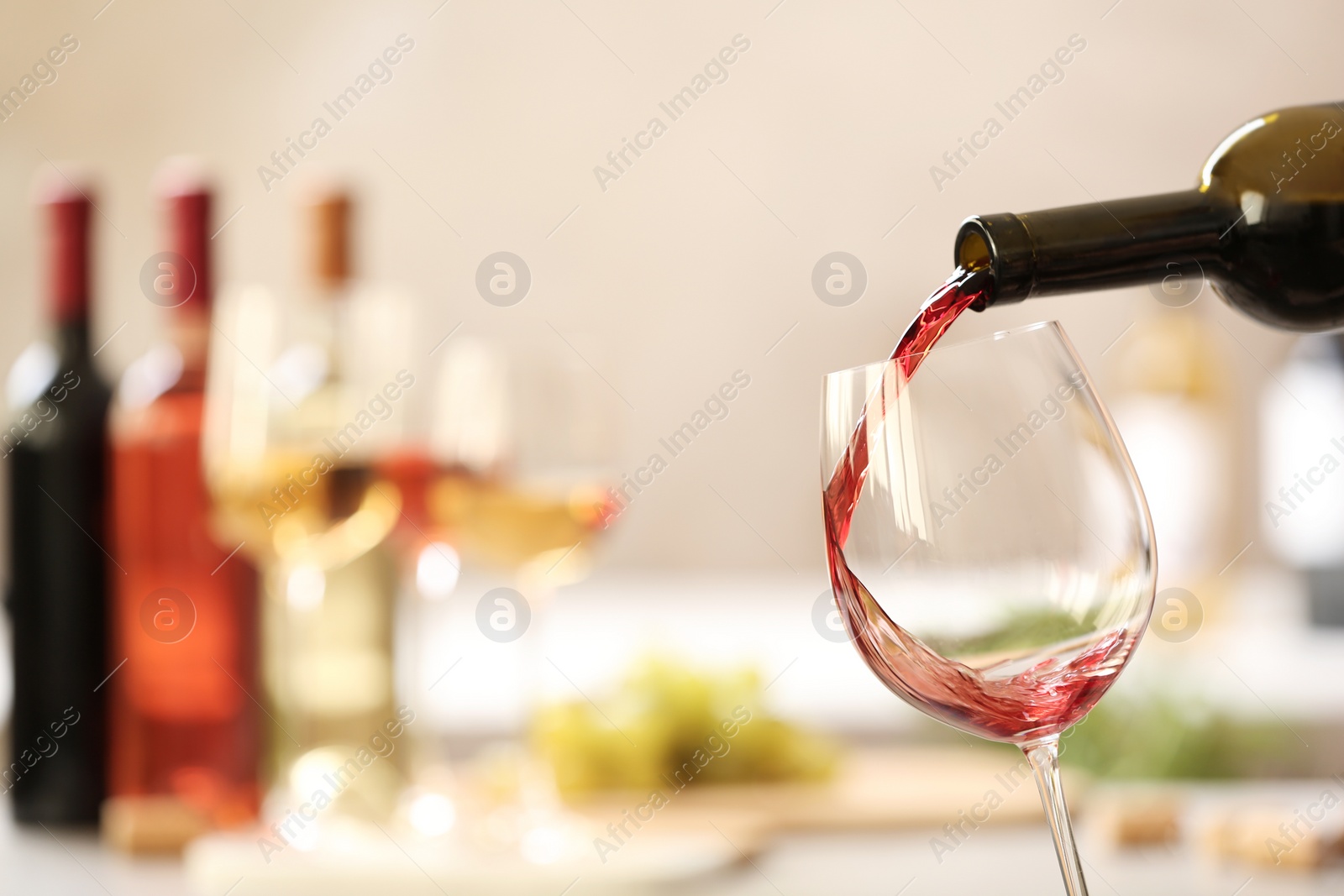 Photo of Pouring red wine from bottle into glass on blurred background. Space for text