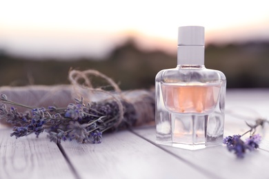 Photo of Bottle of luxury perfume and lavender flowers on white wooden table outdoors. Space for text