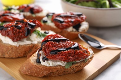 Photo of Delicious bruschettas with sun-dried tomatoes, cream cheese and balsamic vinegar on light table, closeup