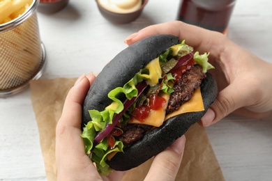 Photo of Woman holding black burger at table, closeup