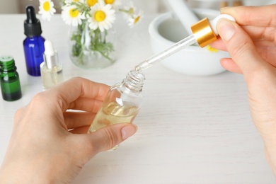 Photo of Woman with pipette and bottle of essential oil at table, closeup