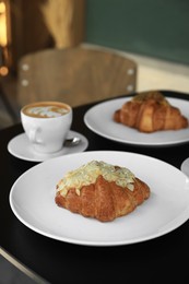 Photo of Tasty croissants and cup of aromatic coffee on black table in cafeteria