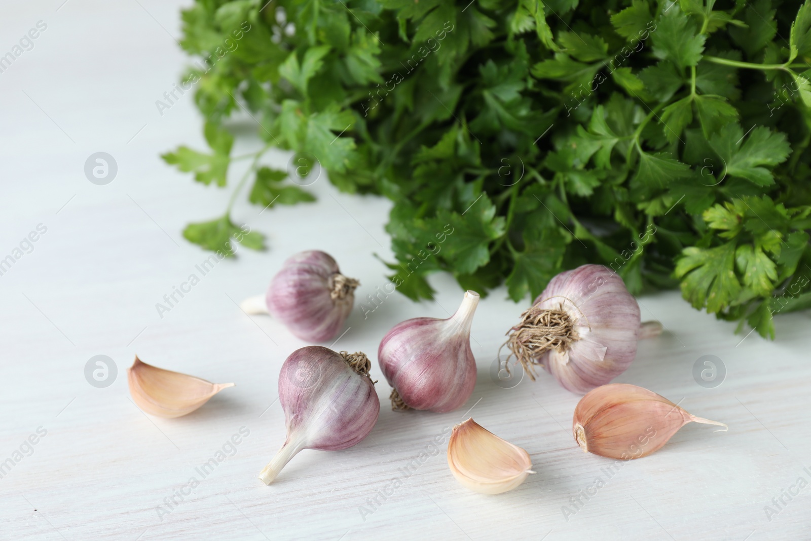 Photo of Fresh raw garlic and parsley on white wooden table, closeup