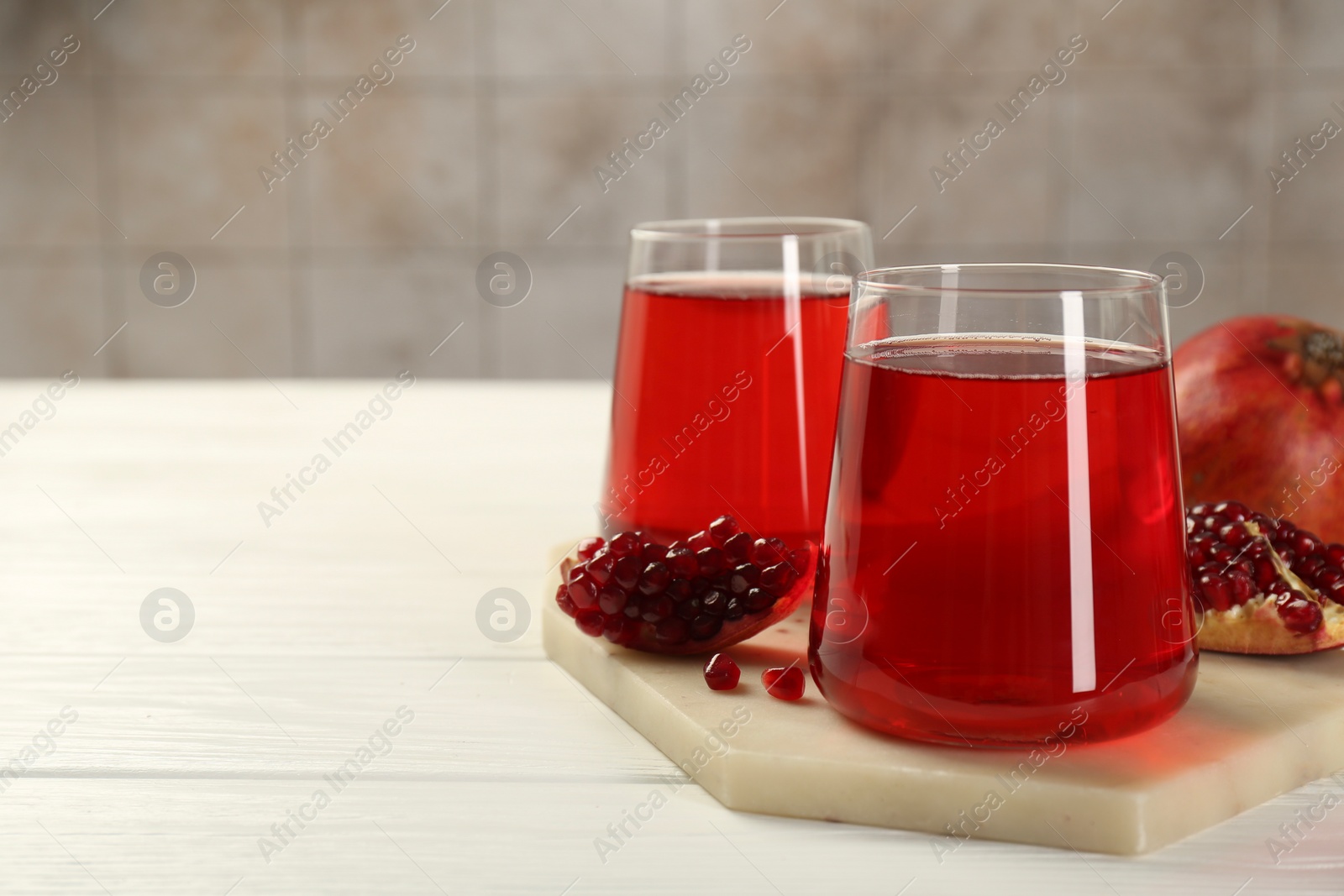Photo of Tasty pomegranate juice in glasses and fresh fruits on white wooden table, closeup. Space for text