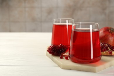 Photo of Tasty pomegranate juice in glasses and fresh fruits on white wooden table, closeup. Space for text