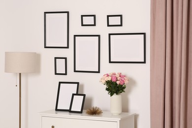 Photo of Empty frames hanging on white wall and chest of drawers with flowers indoors