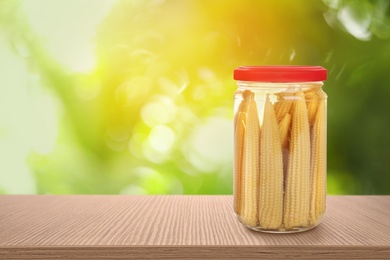 Image of Jar of pickled baby corn on wooden table against blurred background, space for text