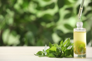 Photo of Dripping nettle oil into glass bottle with leaves on white table against blurred background, space for text