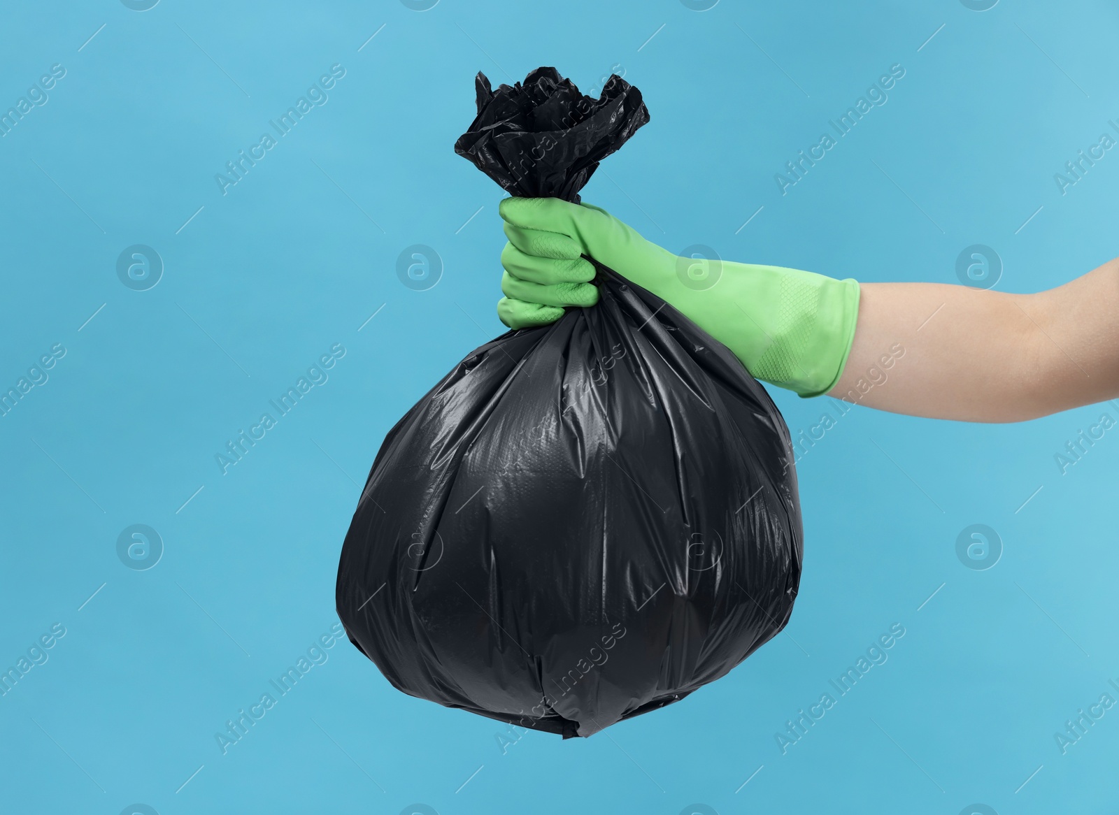 Photo of Woman holding plastic bag full of garbage on light blue background, closeup. Space for text