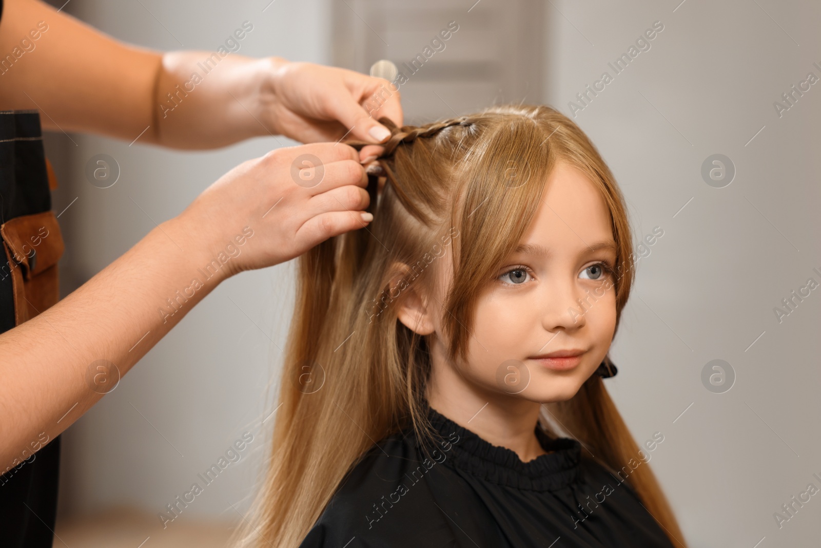 Photo of Professional hairdresser braiding girl's hair in beauty salon, closeup