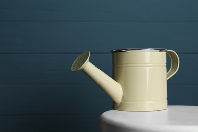 Beige metal watering can on table against blue wooden background, space for text