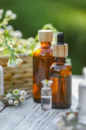 Photo of Bottles of chamomile essential oil and flowers on white wooden table, closeup