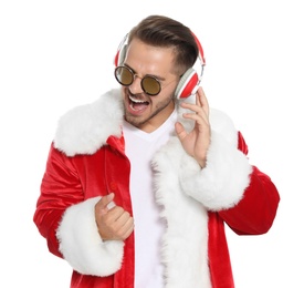 Young man in Santa costume listening to Christmas music on white background