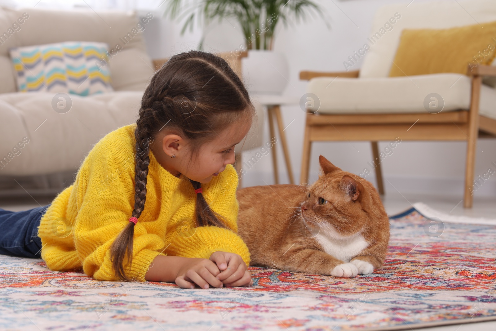 Photo of Little girl and cute ginger cat on carpet at home