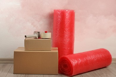 Photo of Red bubble wrap rolls, tape dispenser and cardboard boxes on floor near pink wall