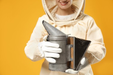 Photo of Beekeeper in uniform holding smokepot on yellow background, closeup