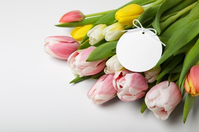 Bouquet of beautiful tulips and blank card on light background, closeup. Birthday celebration