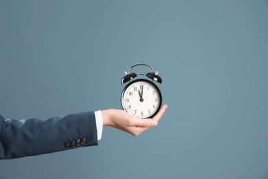 Photo of Young businesswoman holding clock on color background. Time management