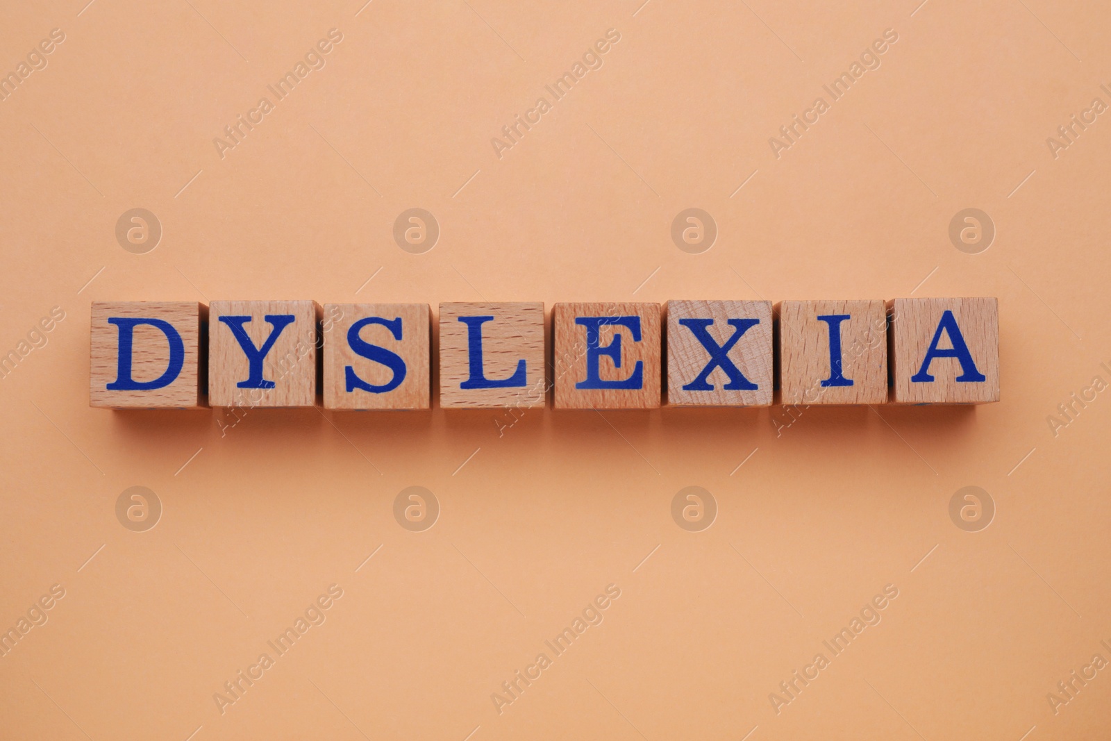 Photo of Wooden cubes with word Dyslexia on pale orange background, flat lay