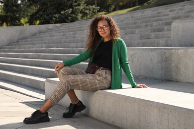 Photo of Beautiful African American woman with stylish waist bag on stairs outdoors