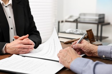 Photo of Senior man signing document in lawyer's office, closeup