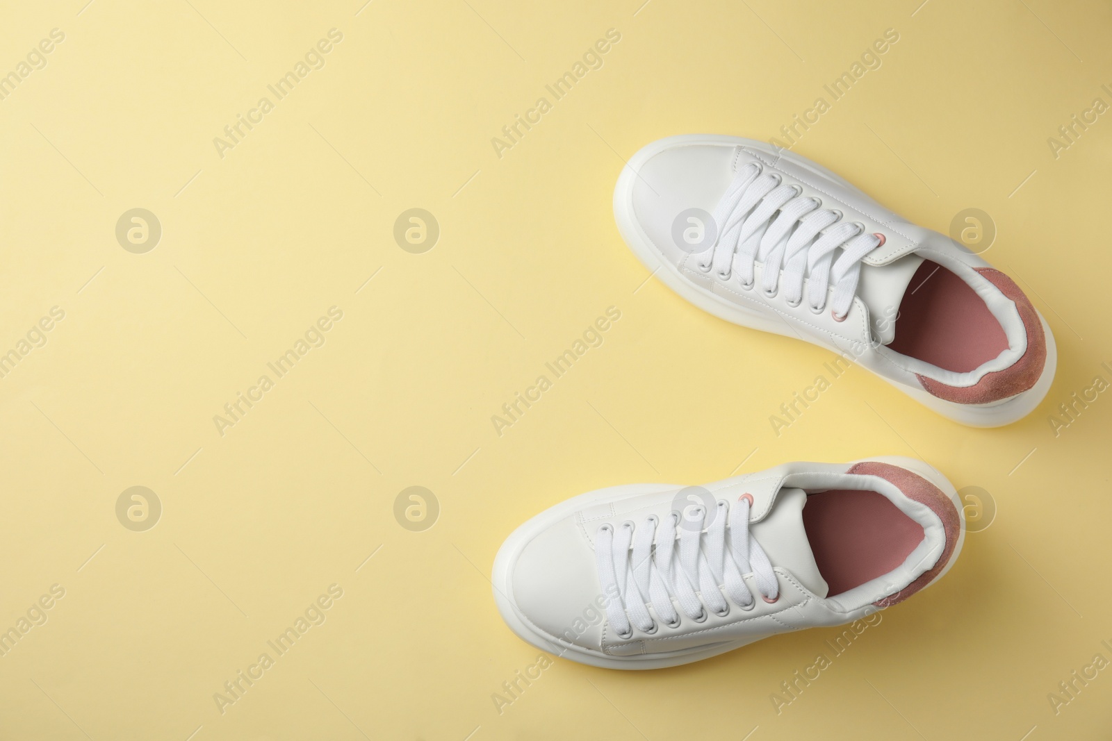 Photo of Stylish white sneakers on pale yellow background, top view. Space for text