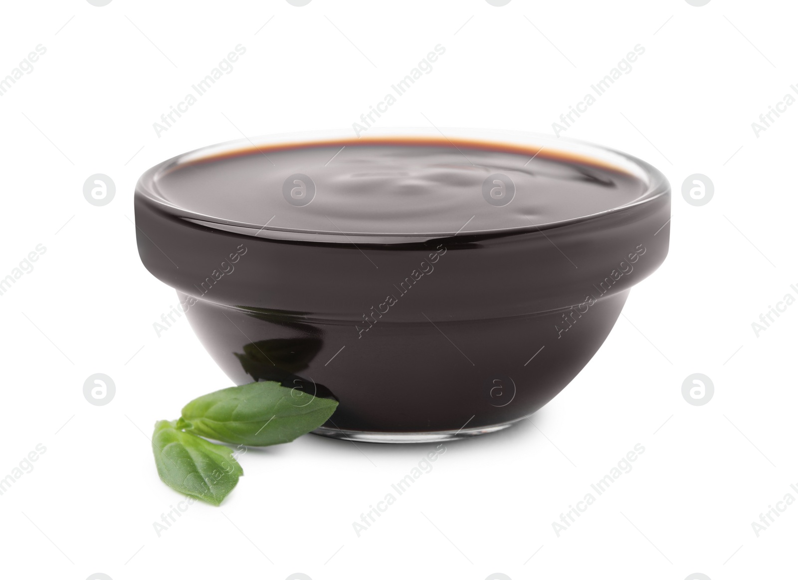 Photo of Glass bowl with balsamic glaze and basil leaves on white background