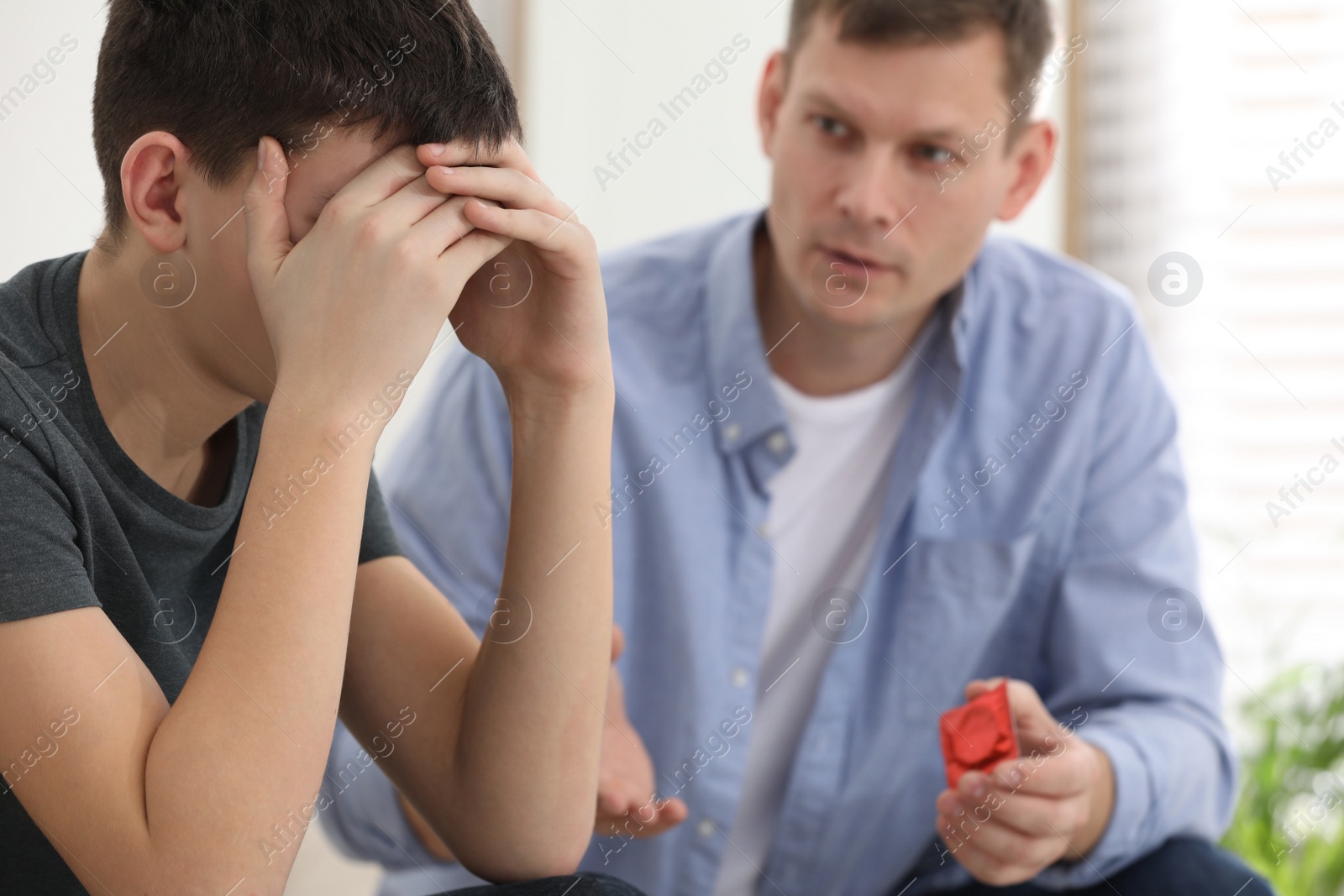 Photo of Father talking with his teenage son about contraception at home. Sex education concept